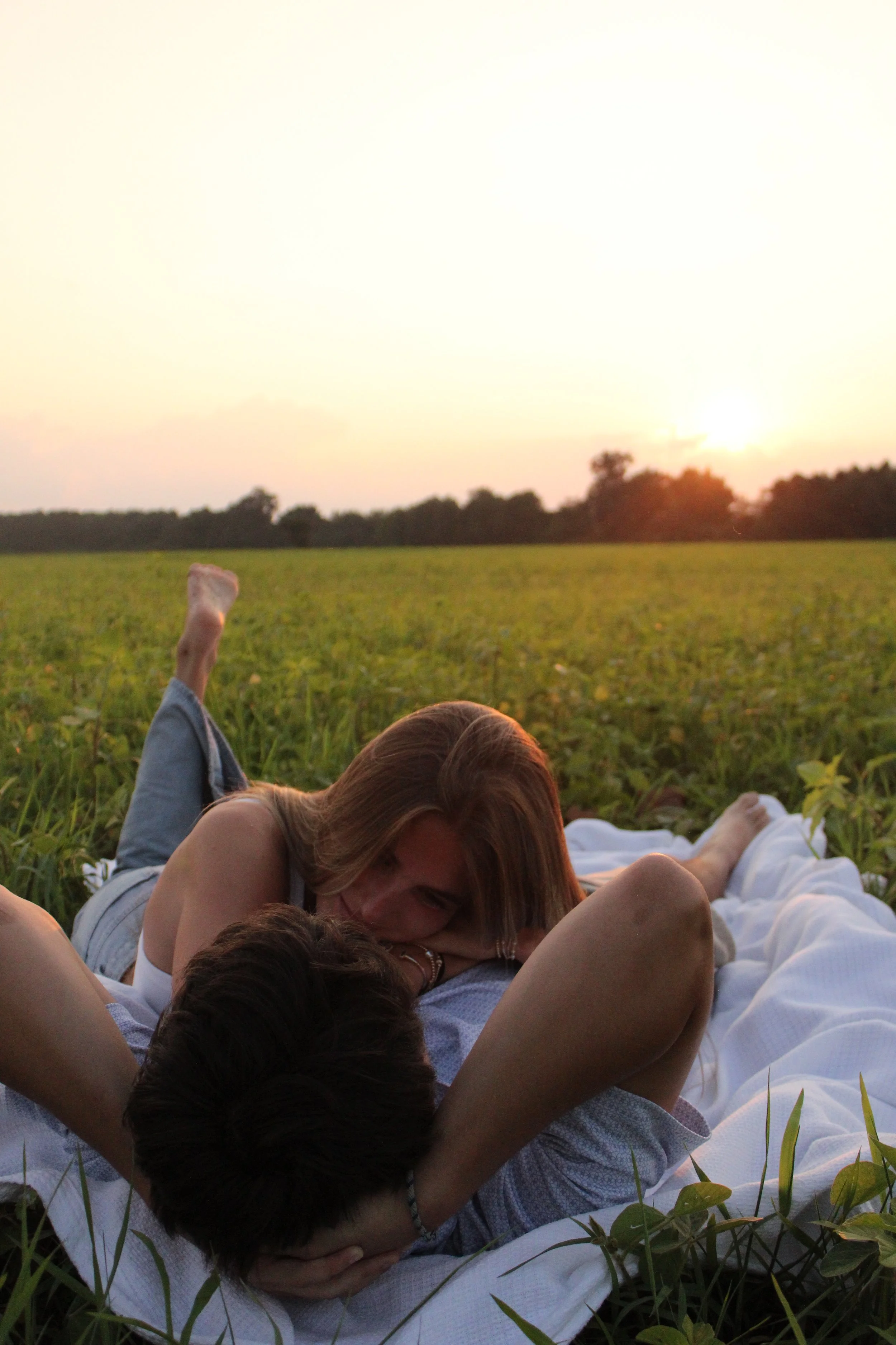 A woman and a young boy are lying on the grass in a field during sunset, with the boy raising his arm and the woman resting peacefully.