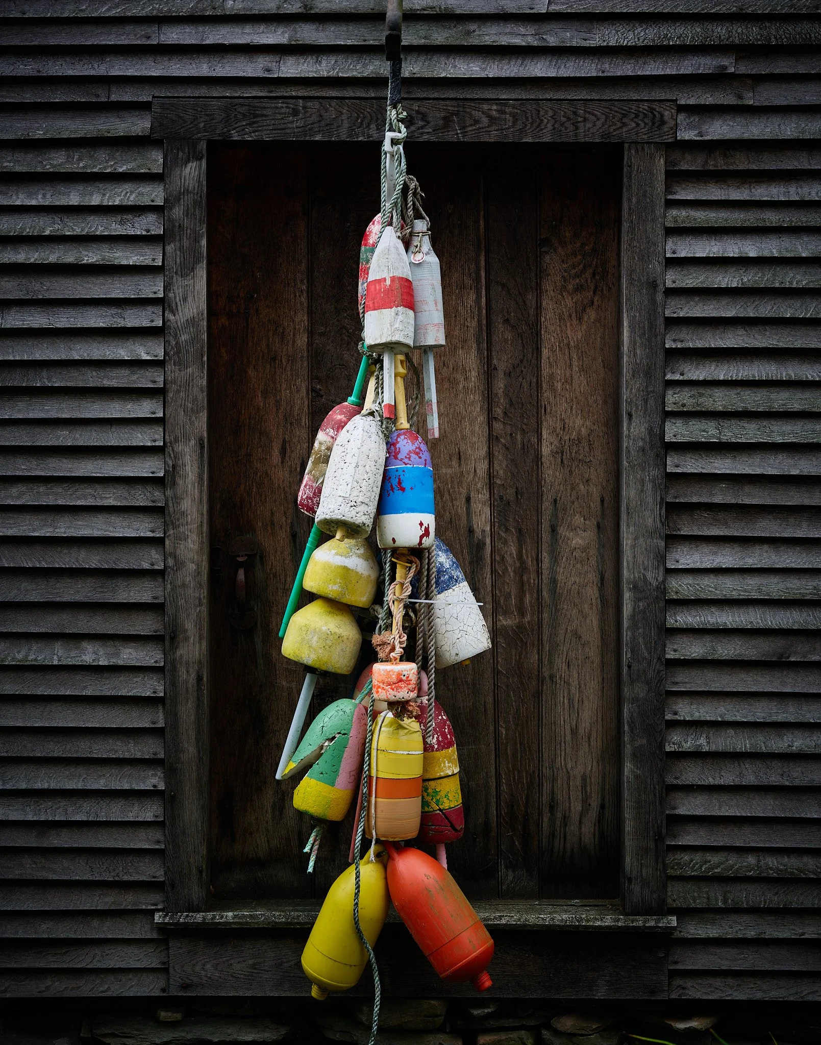 Colorful fishing buoys hanging on a rope against a wooden wall.