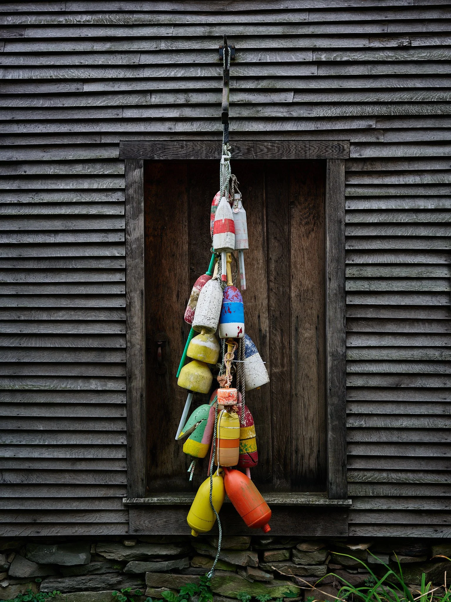 A collection of colorful buoys hanging on a rope in front of a rustic wooden wall.
