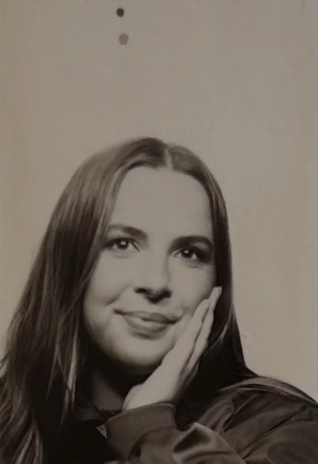 Black and white portrait of a young woman with long hair, smiles gently, and rests her face on her hand.