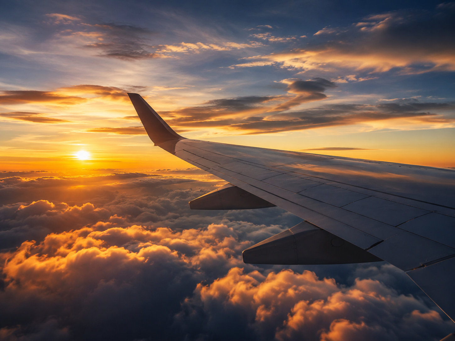 View from an airplane window showing the wing and a sunset sky above the clouds.