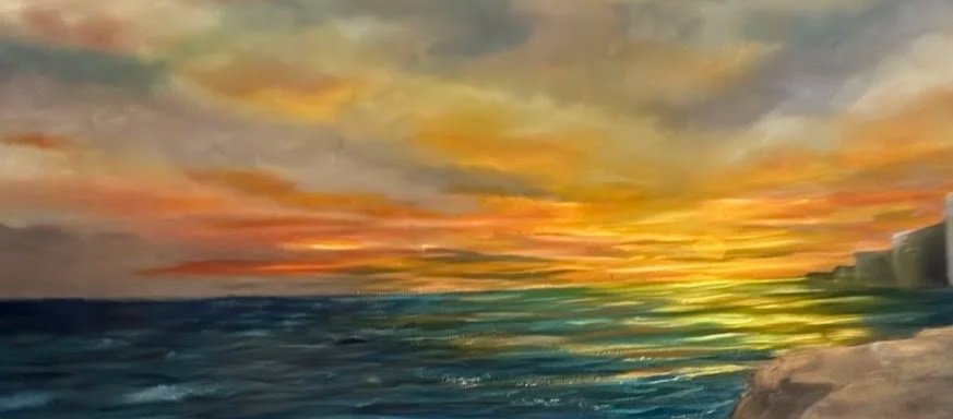Colorful sunset over a calm ocean with some clouds in the sky.