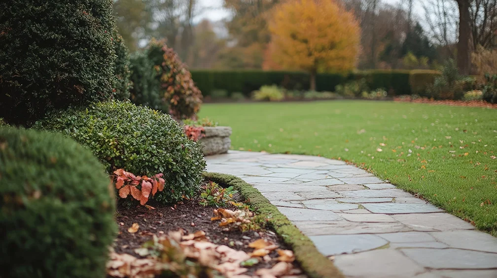 A curved stone pathway running through a well-maintained lawn with autumn-colored trees and bushes in the background.