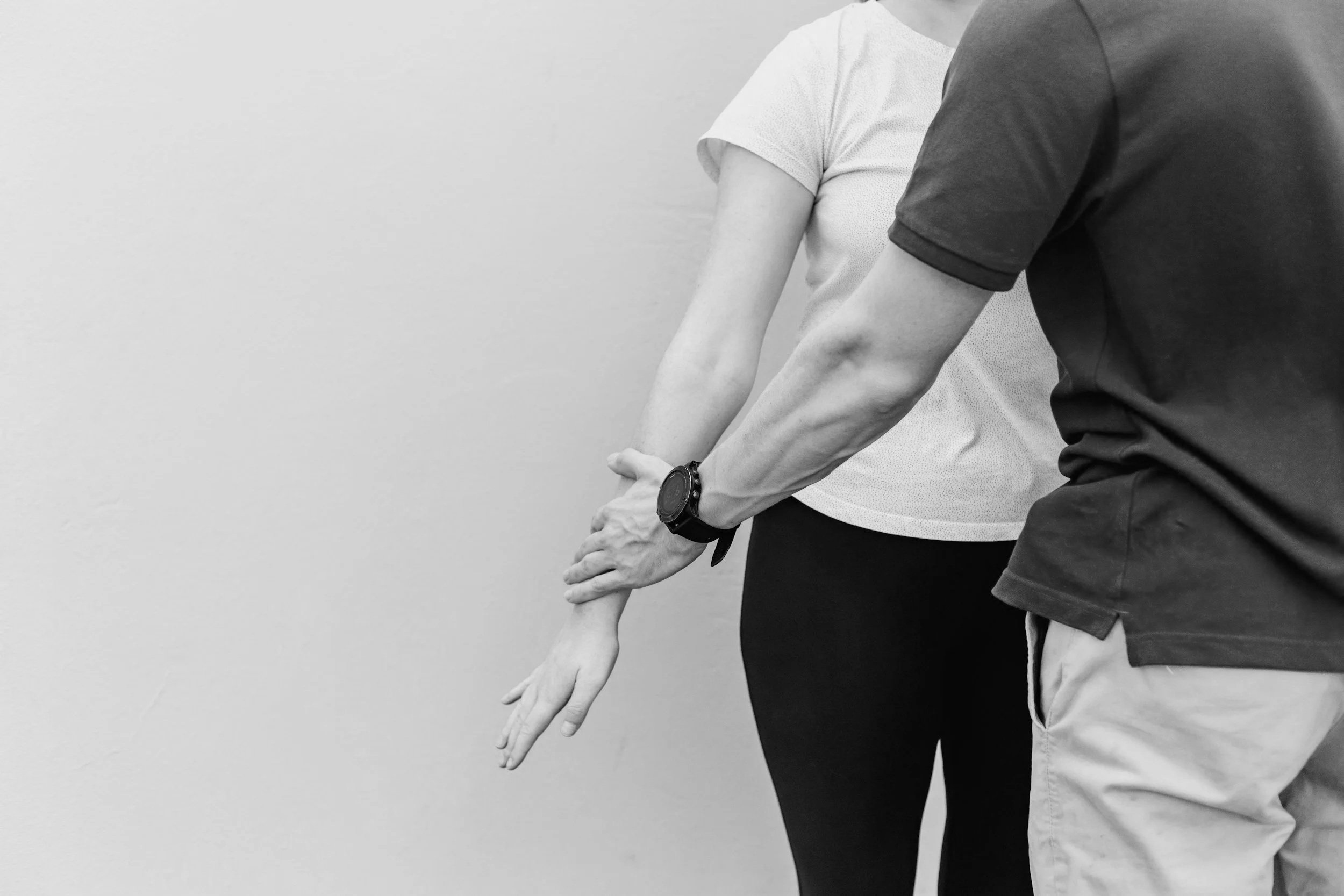 Close-up of two people in a stretching or exercise pose, showing their arms extended and hands pointing downward.