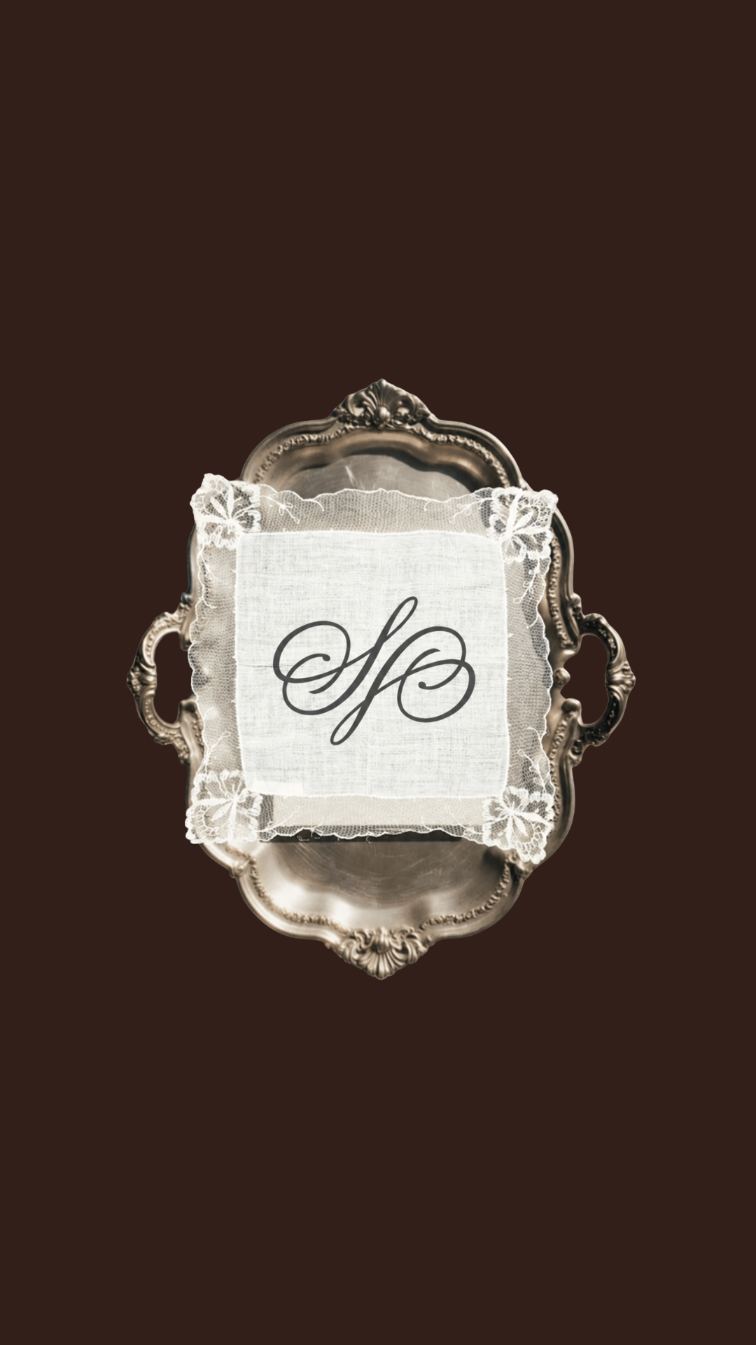 A decorative silver tray with ornate handles and edges, holding a lace handkerchief with the letter 'S' embroidered in cursive, placed on a dark background.