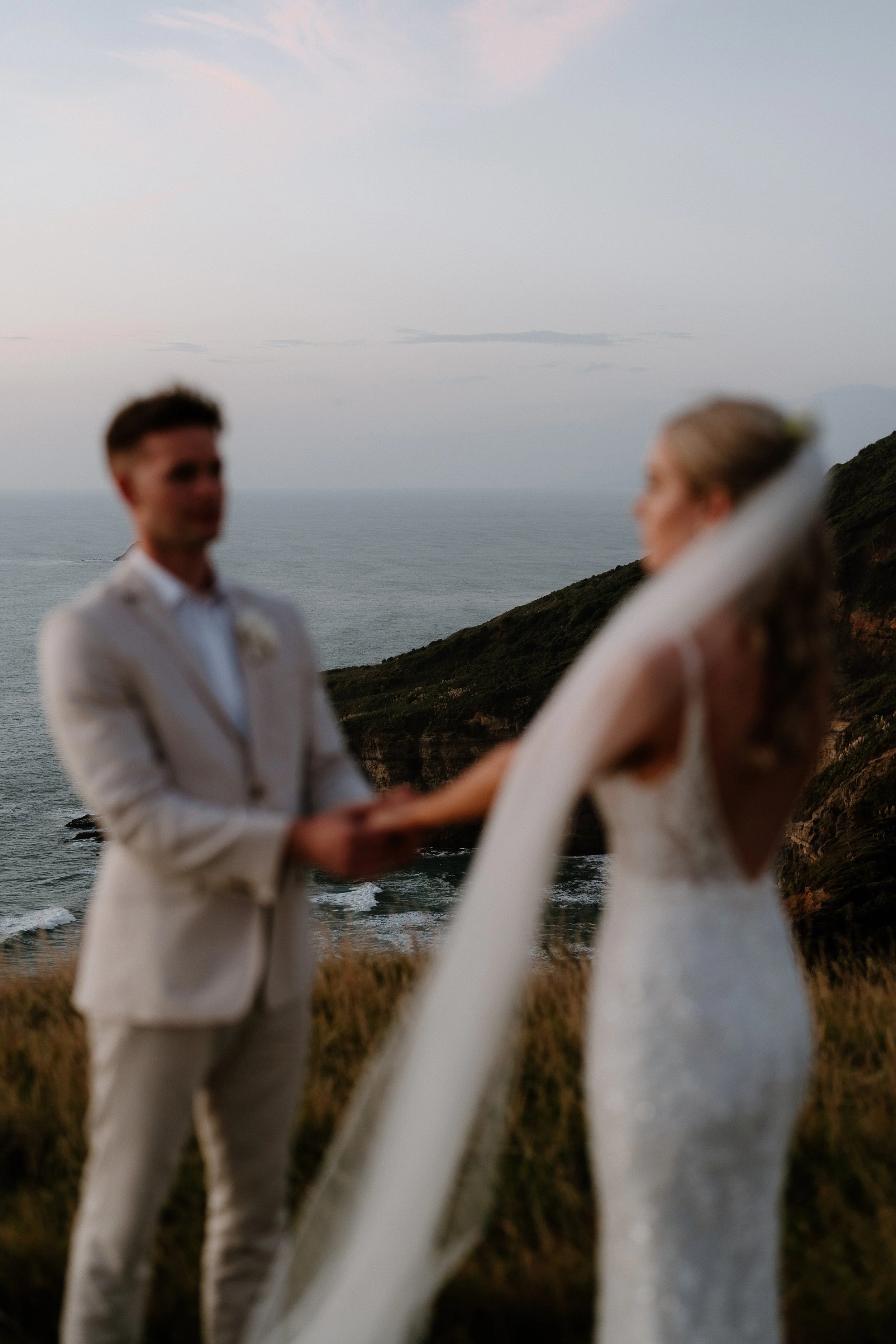Blurry couple in white clothing standing on a coastal cliff overlooking the ocean.