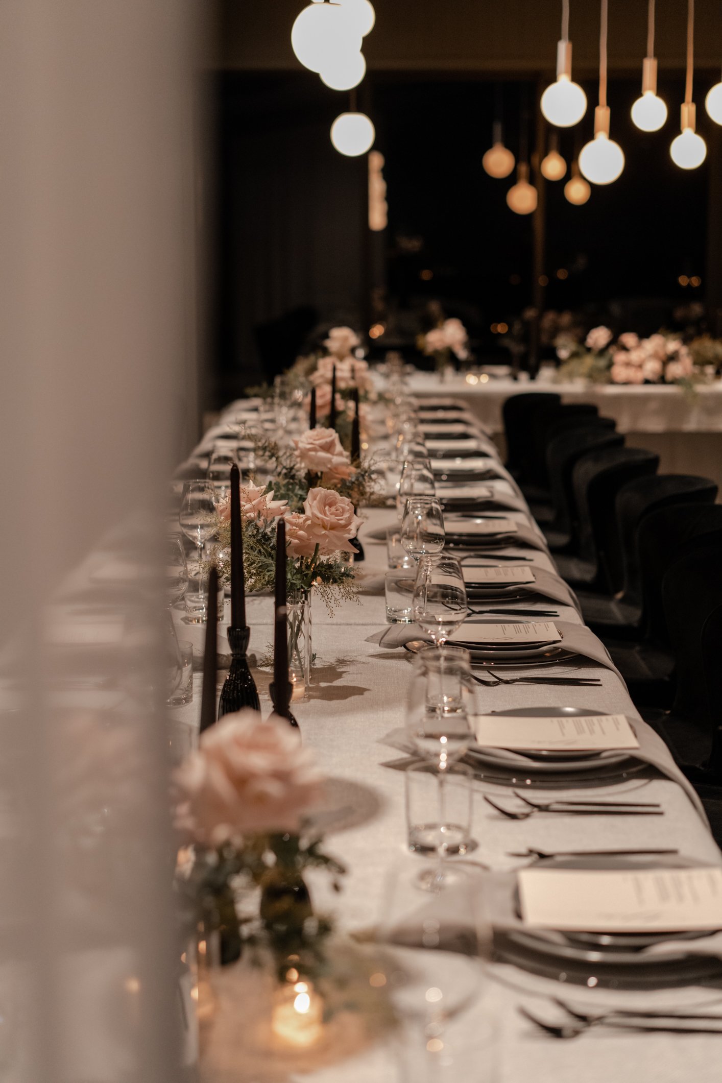 Elegant dinner table set with black chairs, floral centerpieces, candles, place settings, and hanging globe lights