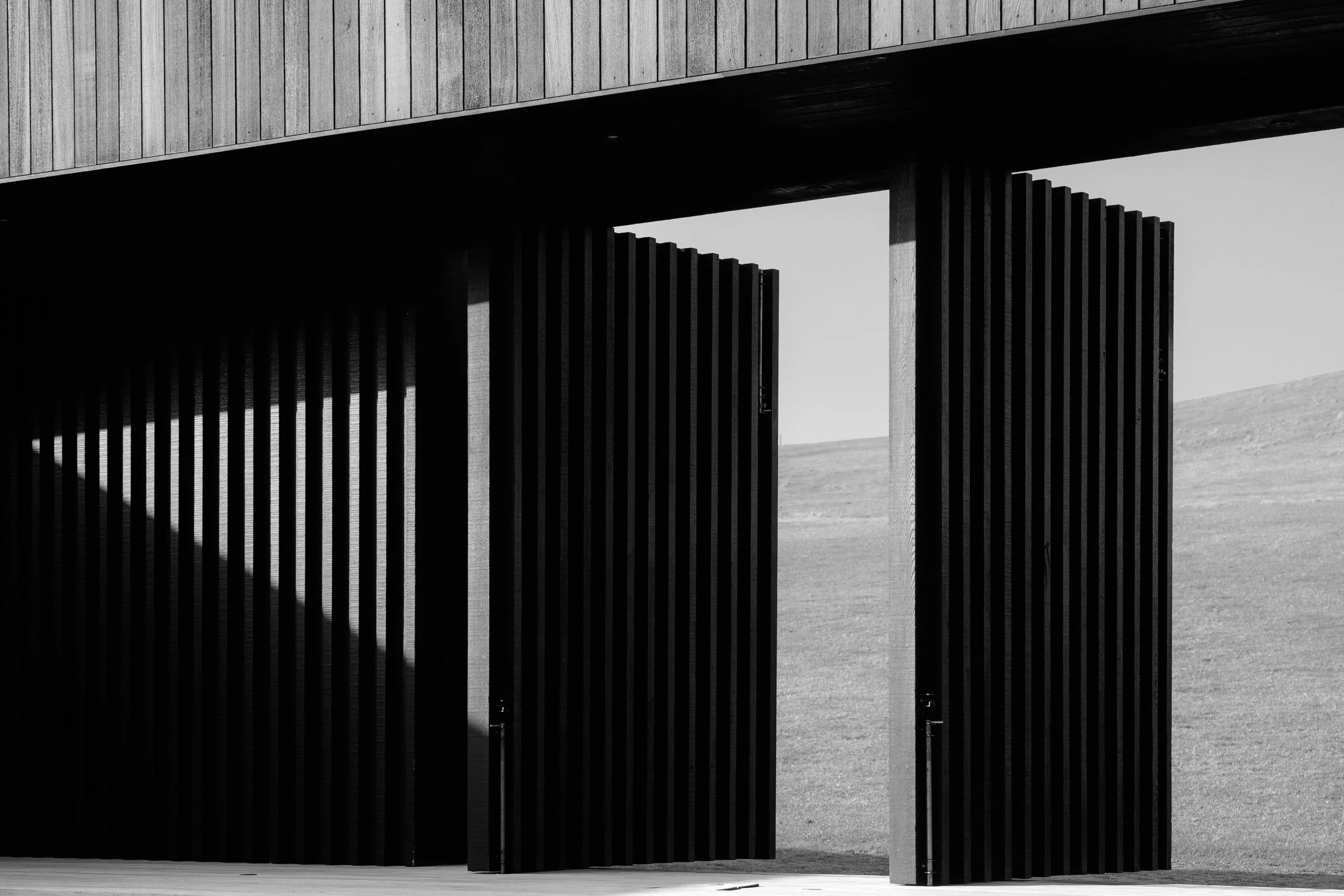 Black-and-white architectural view of a modern building with tall ribbed walls framing rolling hills