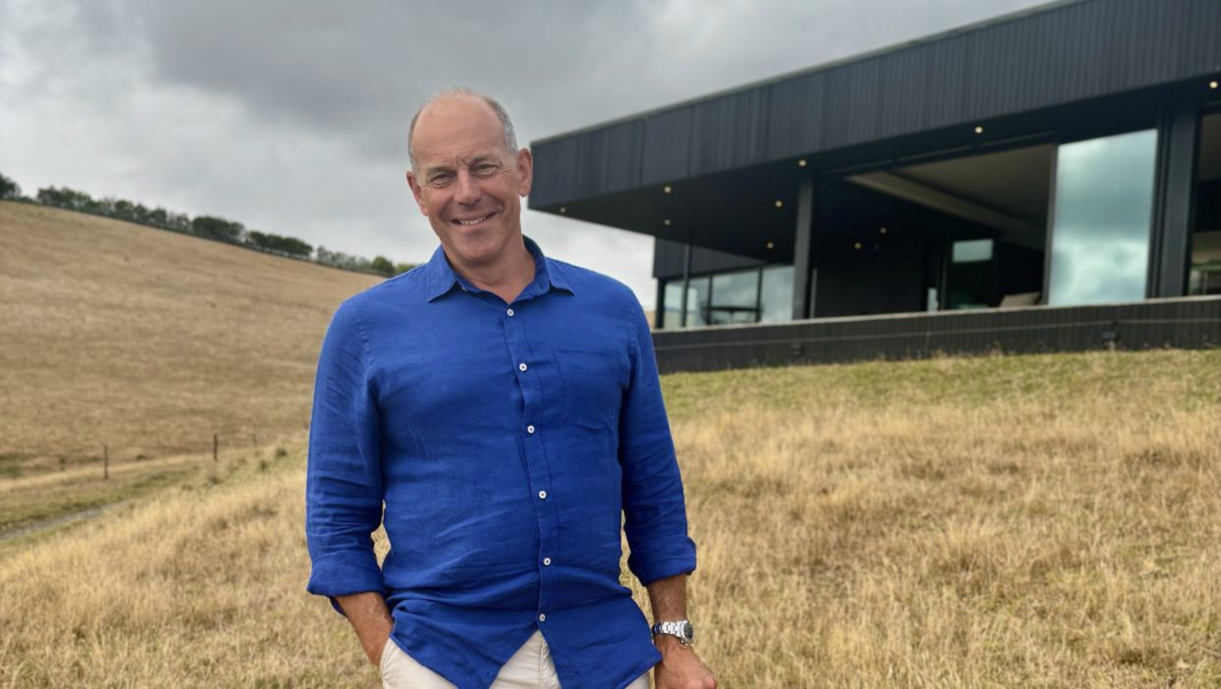Smiling man in a blue shirt standing in a grassy field outside a modern black building