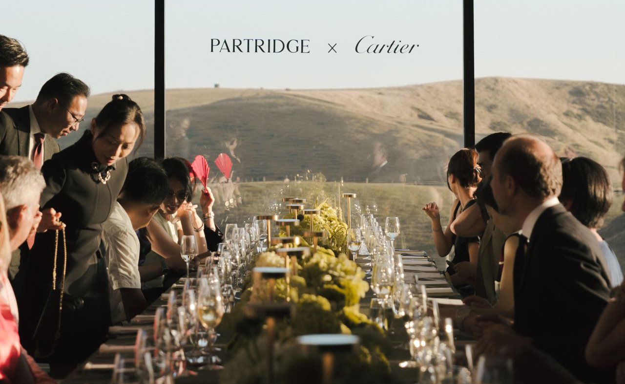Partridge x Cartier dinner party with guests seated at a long table overlooking rolling hills