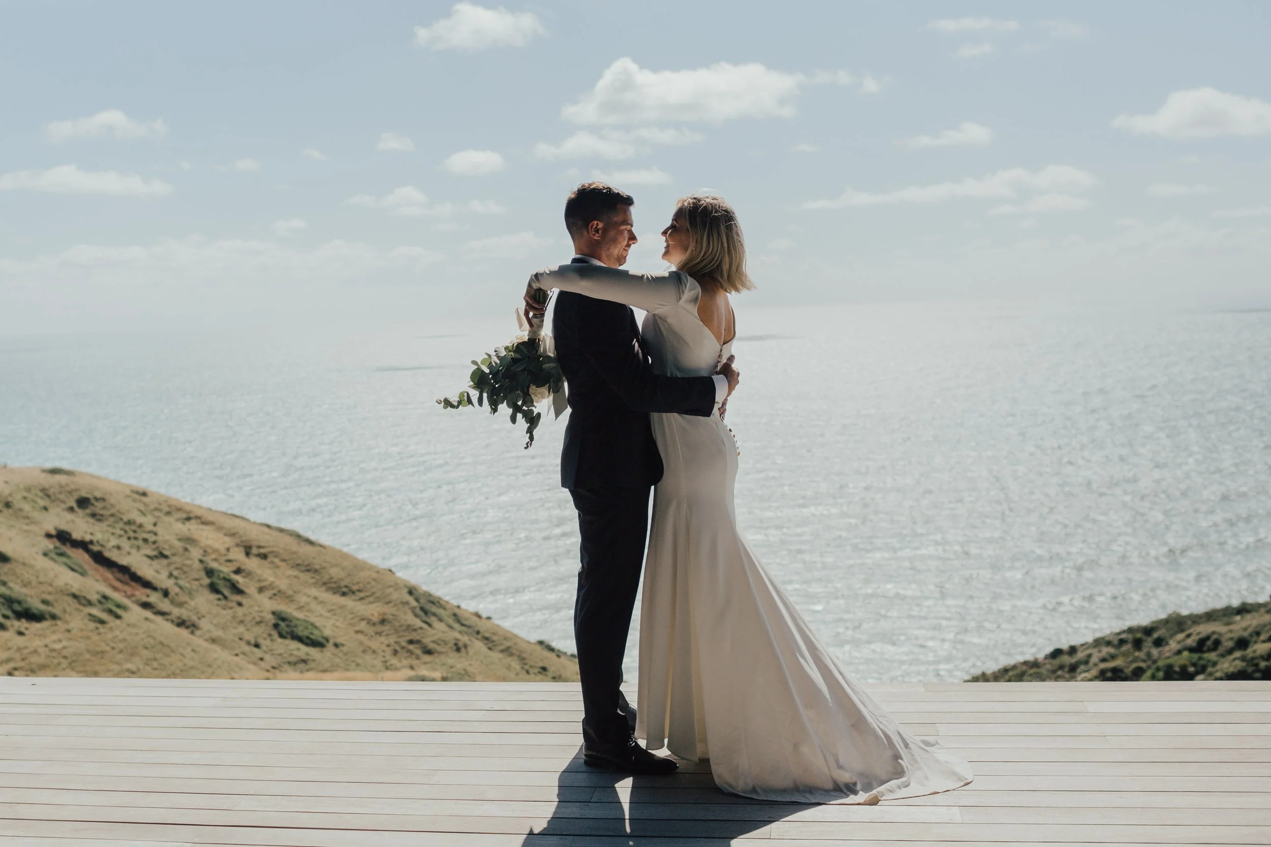 Bride and groom embracing on a seaside deck overlooking the ocean