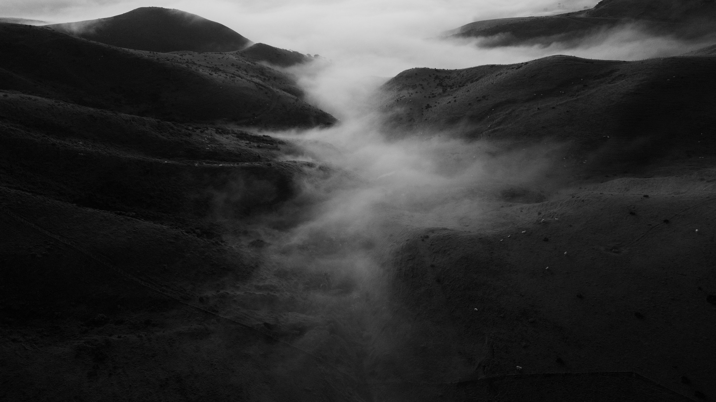 Black-and-white landscape of fog drifting through rolling mountain hills