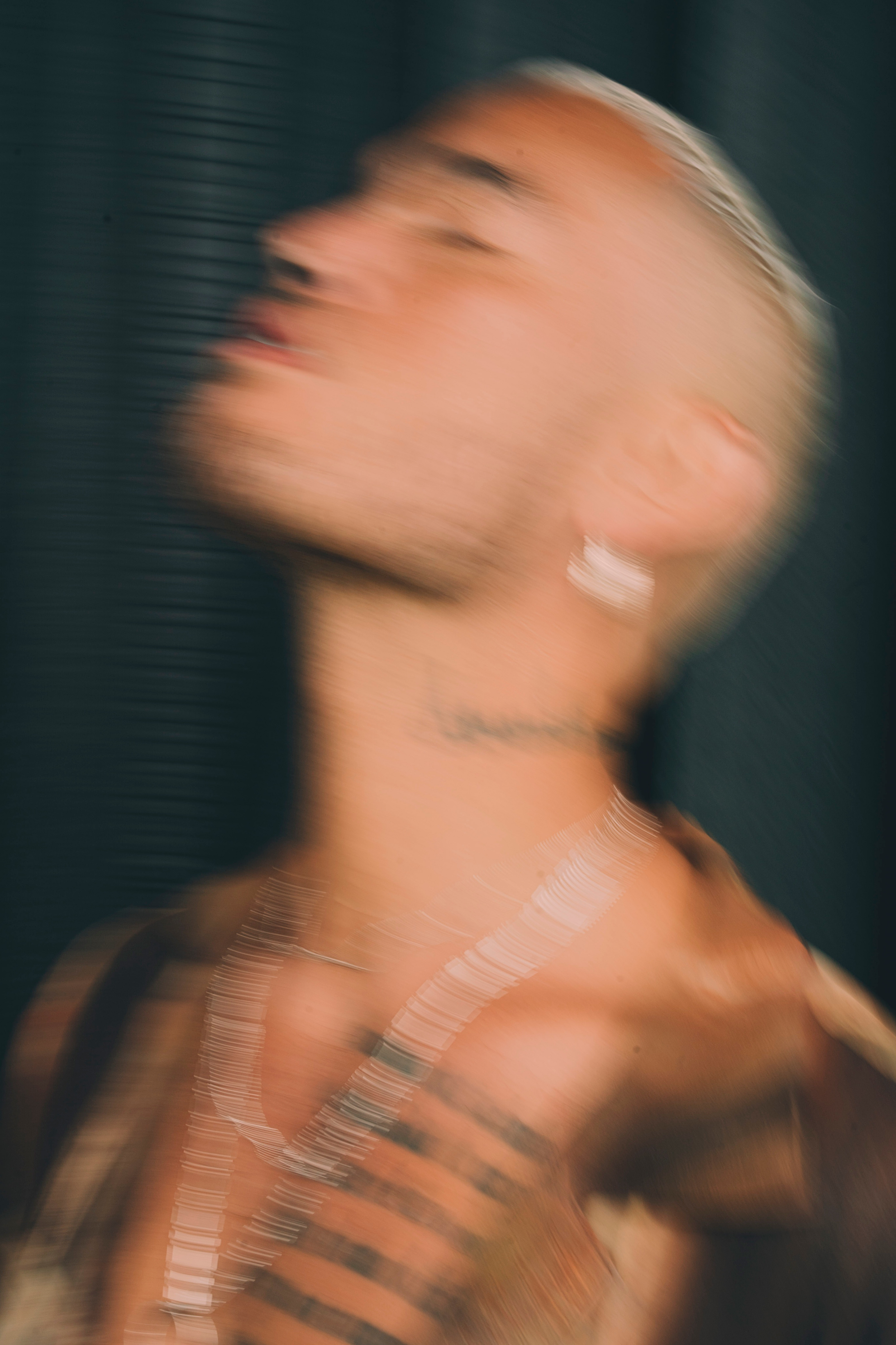 Motion-blurred close-up portrait of a tattooed man with bleached hair against a dark background