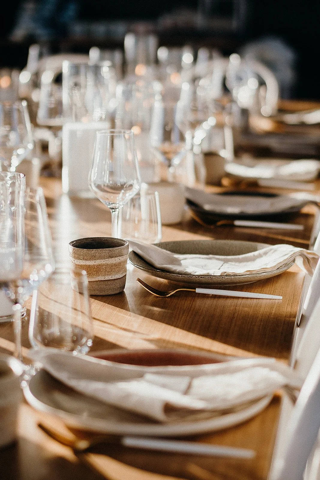 Elegant restaurant table set with plates, folded napkins, wine glasses, ceramic cups, and gold-handled flatware