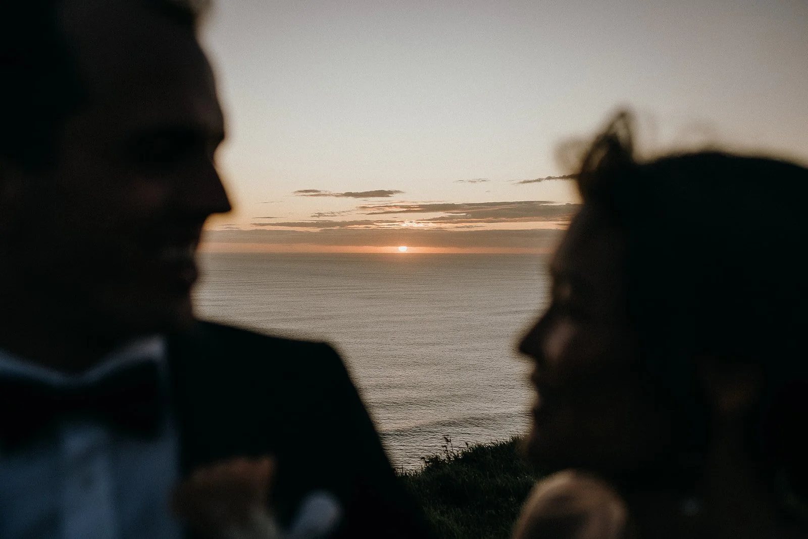 Silhouetted couple facing each other with an ocean sunset between them