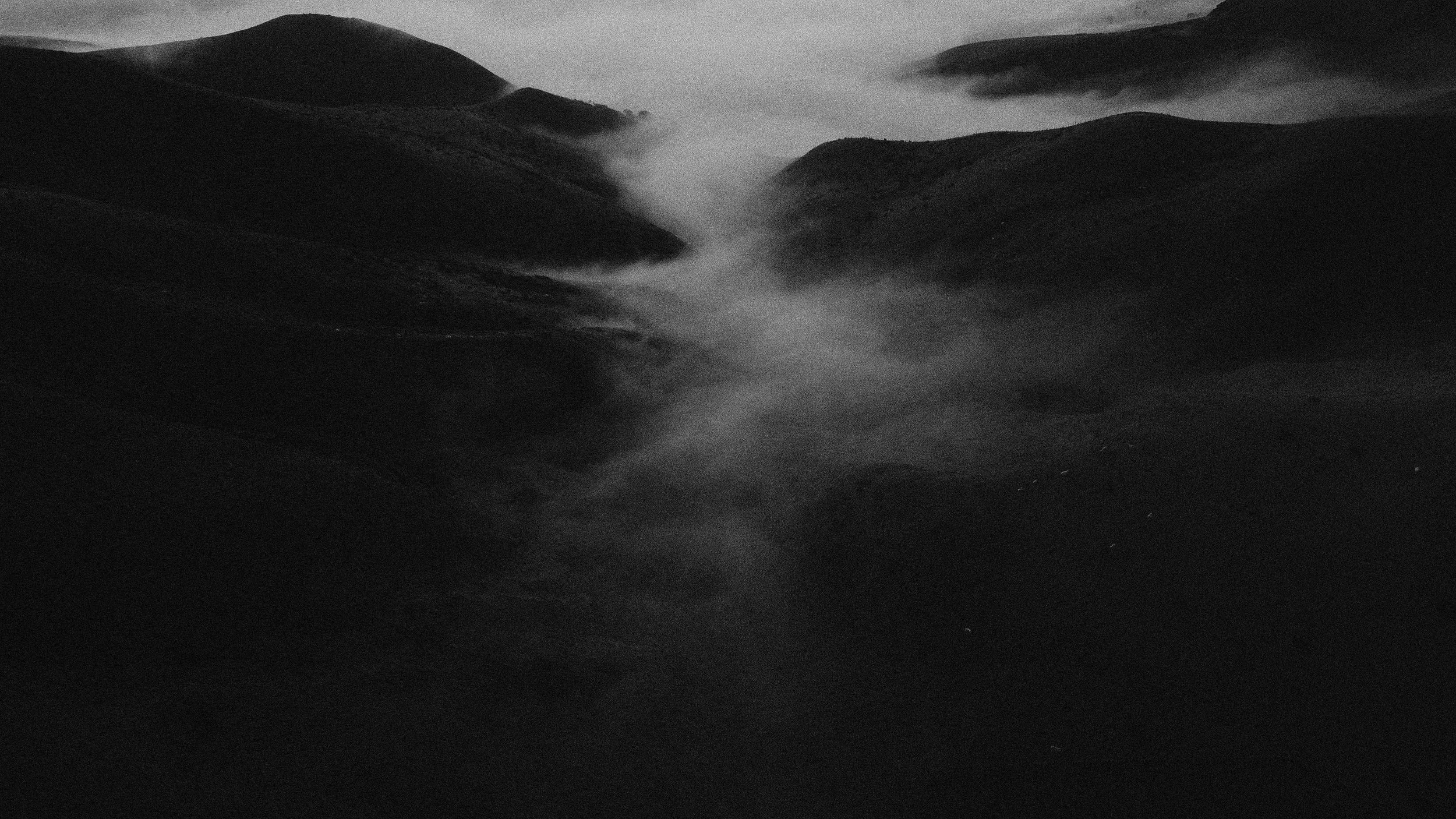 Black-and-white mountain landscape with mist drifting through a valley