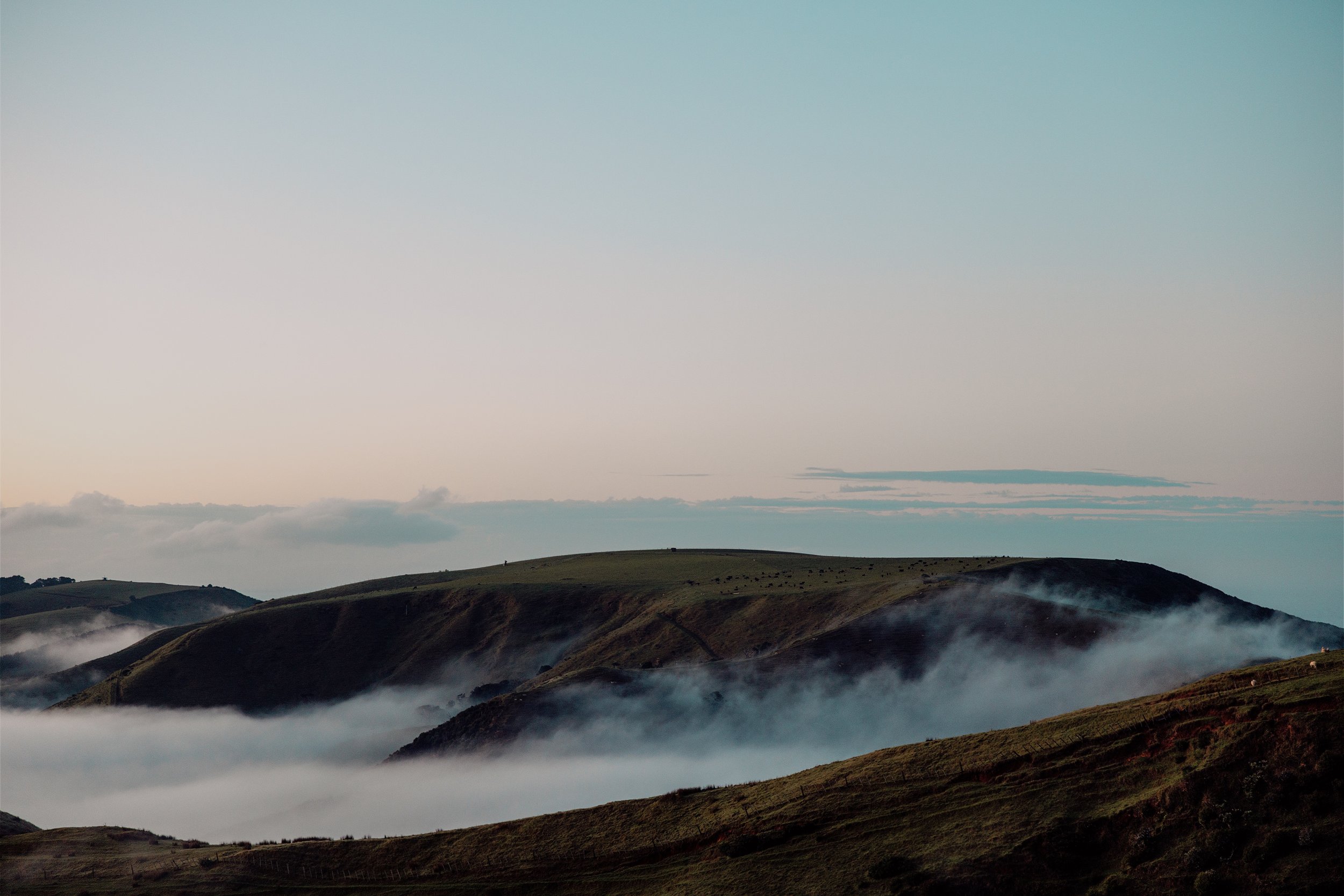 Rolling green hills covered in mist beneath a pastel blue and pink sky