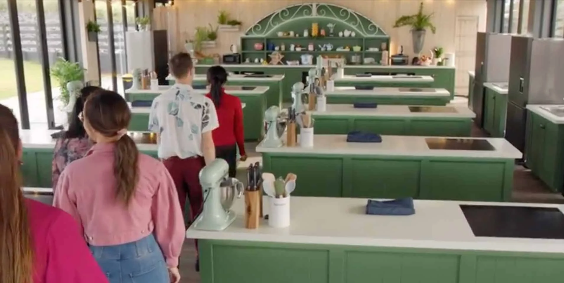 Group touring a bright green commercial kitchen with islands, stand mixers, and cookware displays