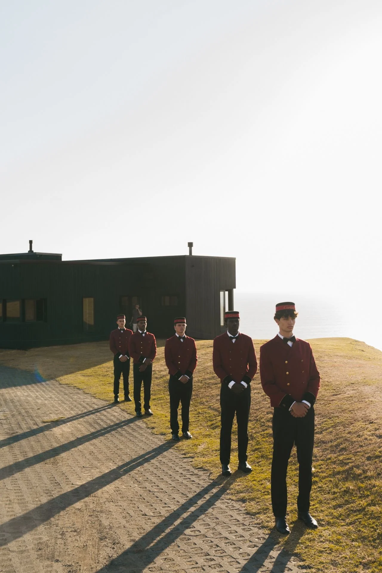 Five uniformed staff standing outside a modern seaside building overlooking the ocean