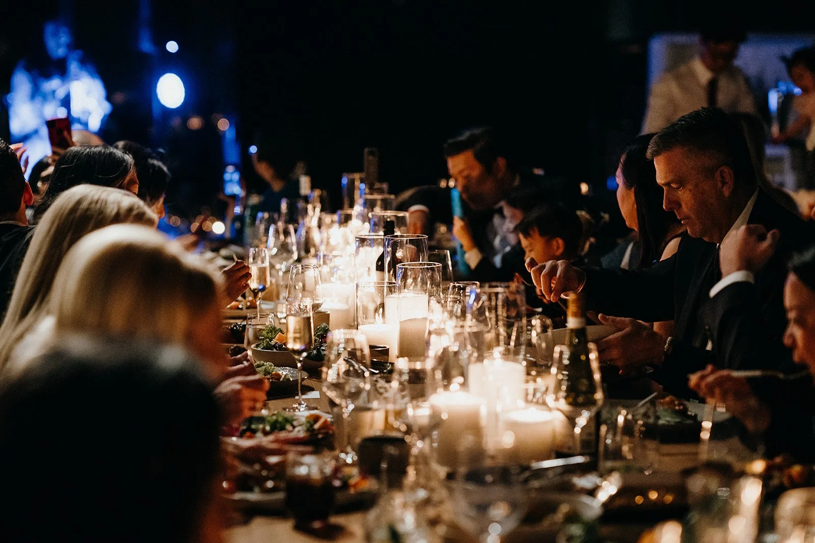 Guests dining at a long candlelit dinner table in a dimly lit restaurant