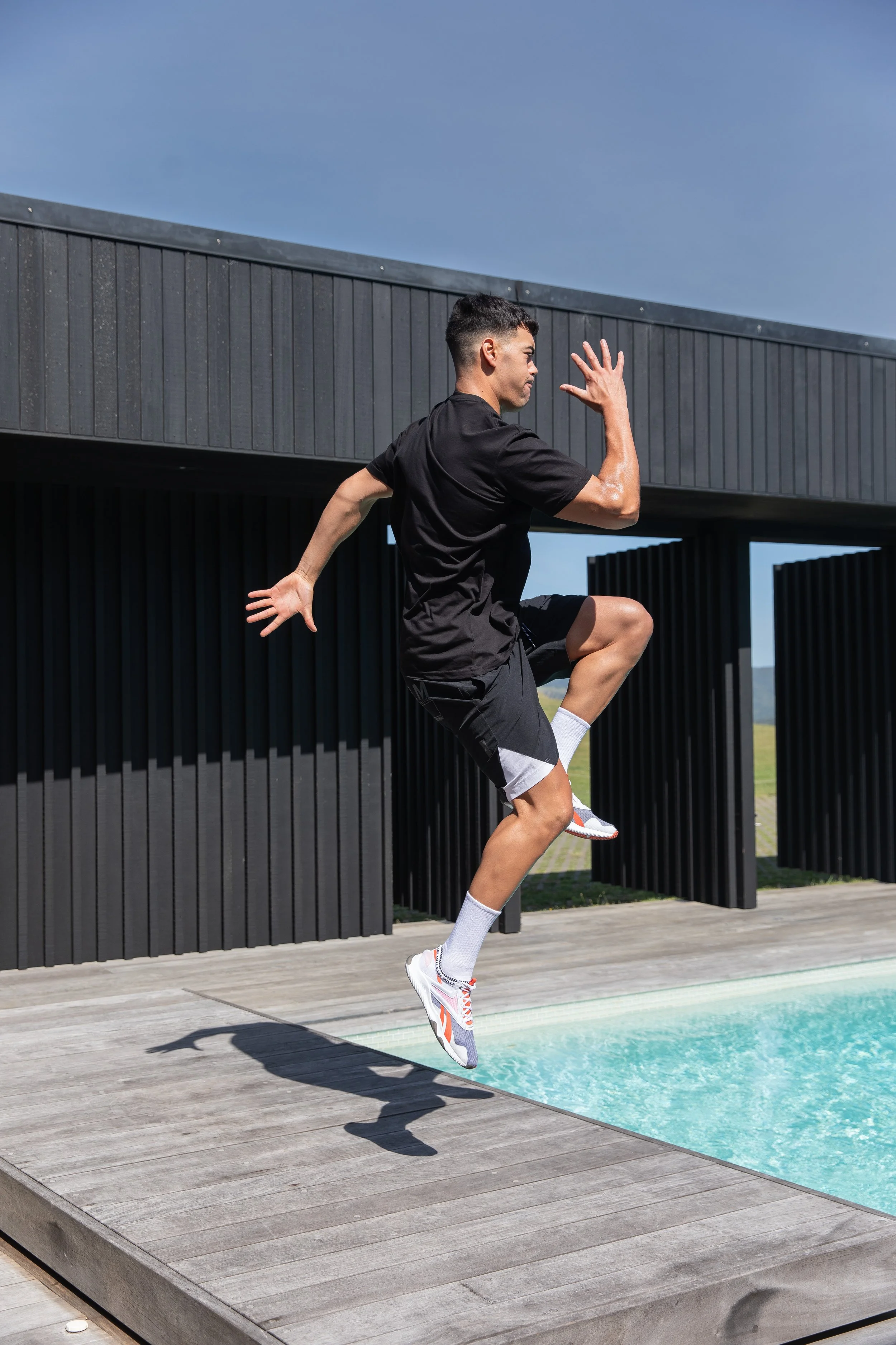 Athletic man in black sportswear leaping beside a swimming pool on a sunny day