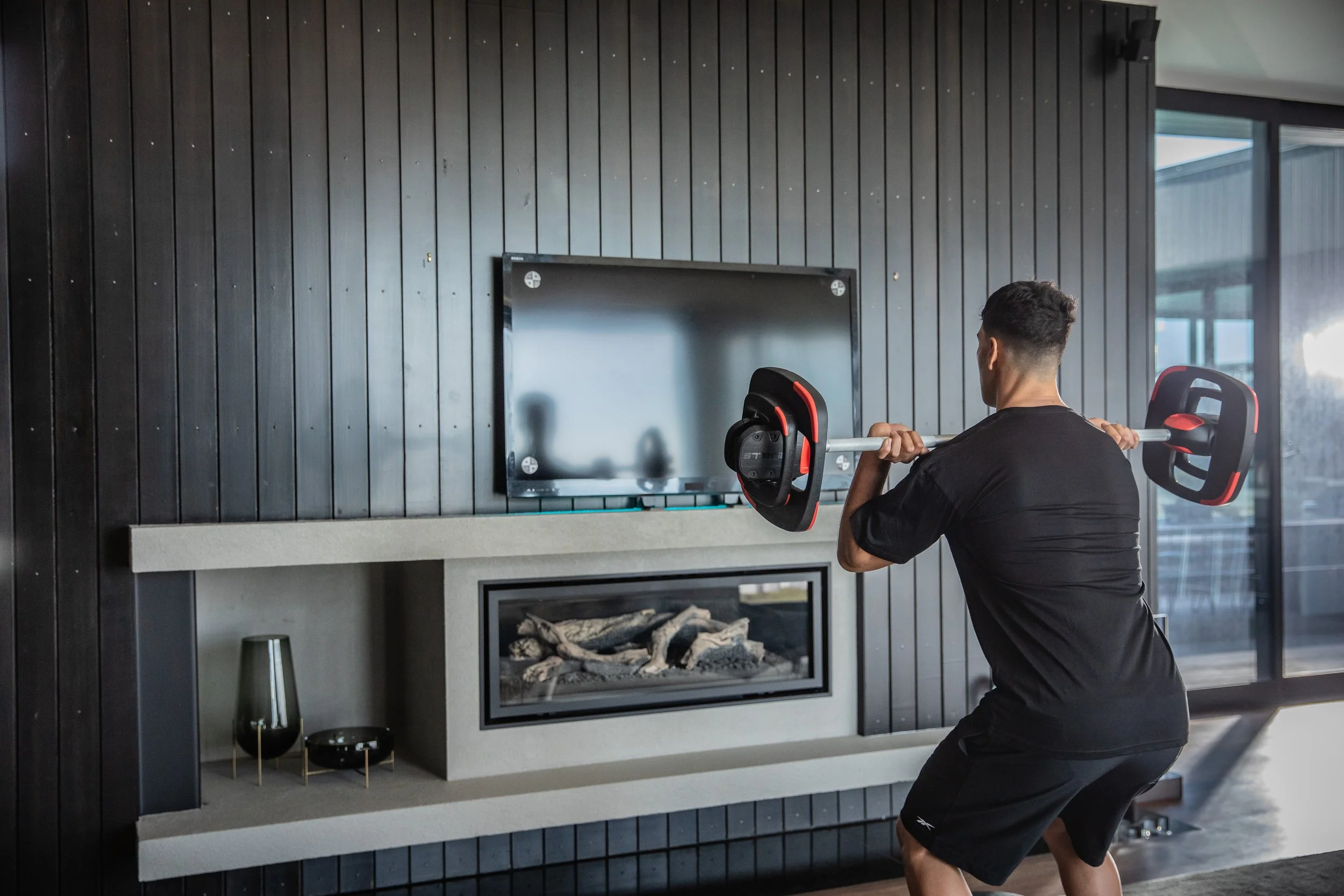 Man performing a barbell squat in a modern home gym and living room