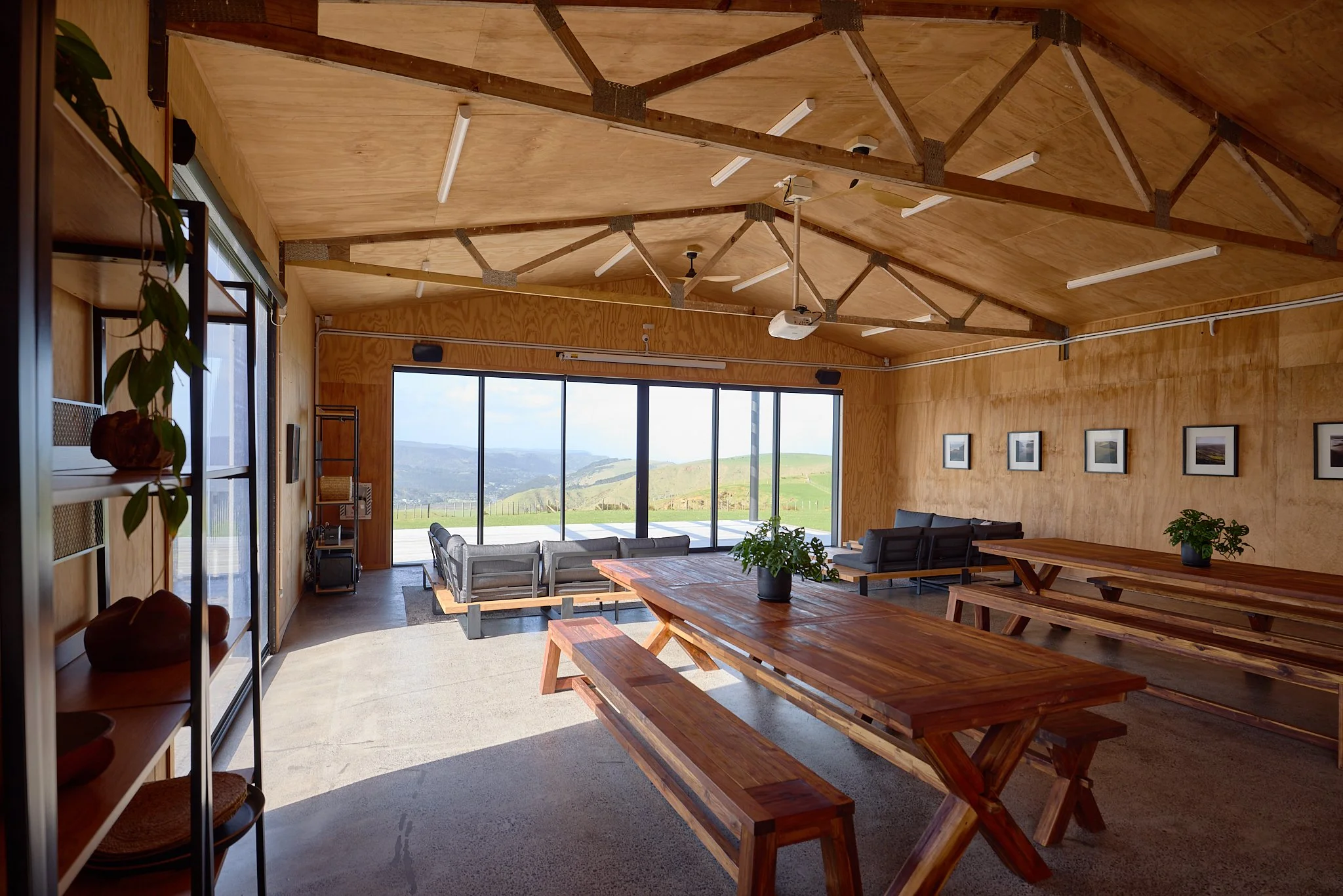 Wood-paneled lodge dining room with picnic tables, lounge seating, large windows, and mountain views