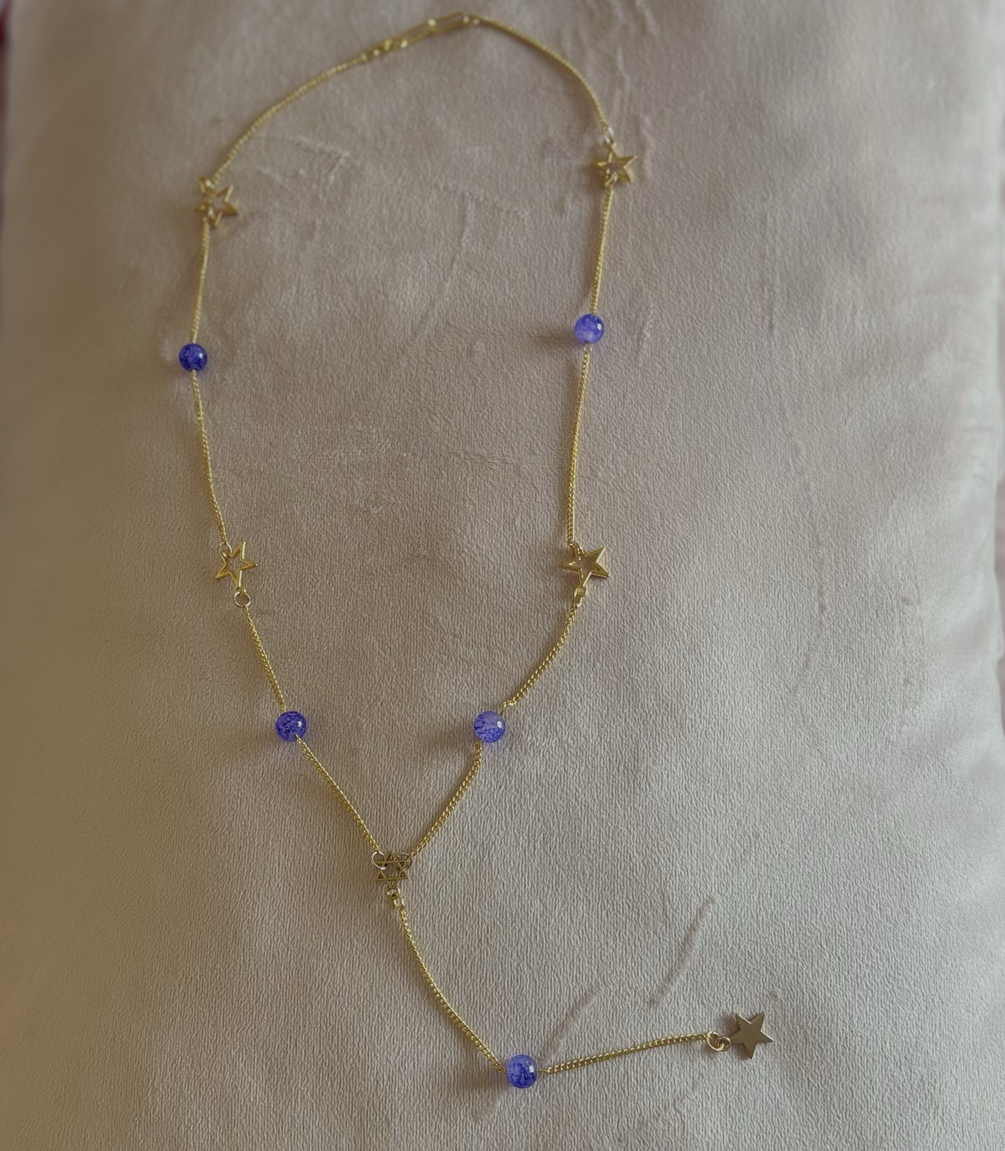 Gold necklace with star charms and purple beads displayed on a beige surface.