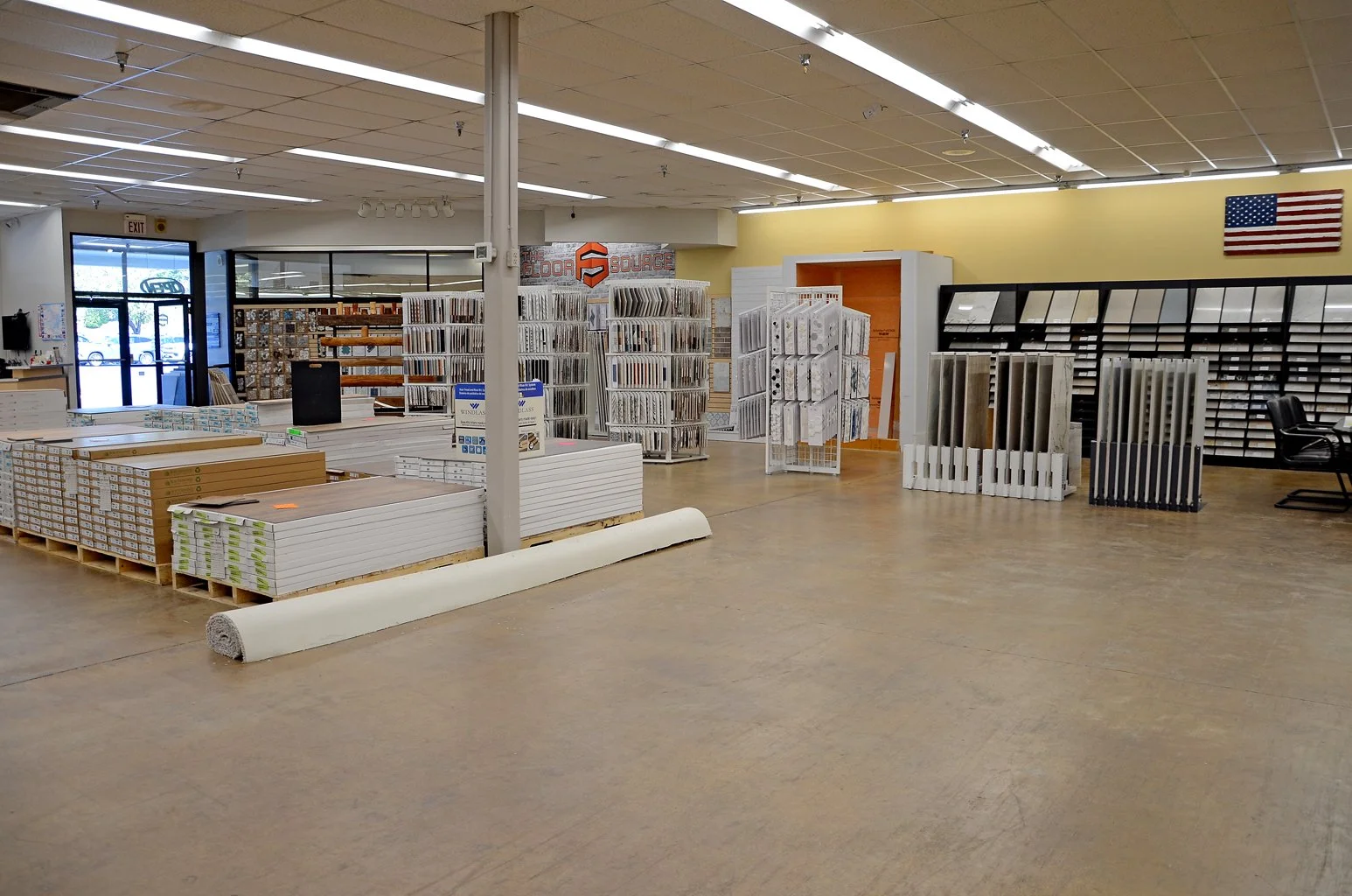 Interior of a flooring store with display samples of flooring and baseboards, near the entrance, with an American flag on the wall.