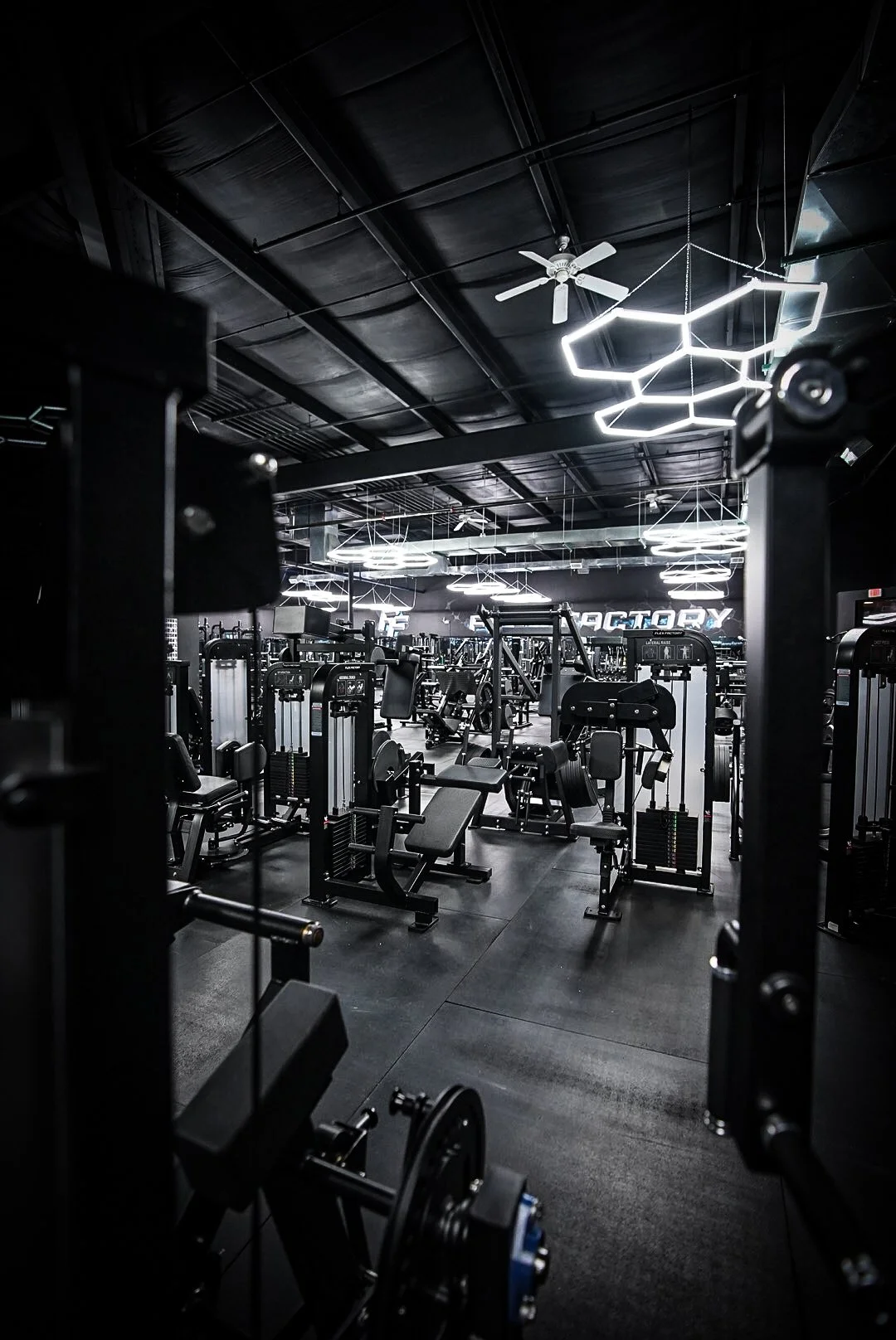 Interior of a modern gym with various workout equipment and hexagon-shaped ceiling lights.