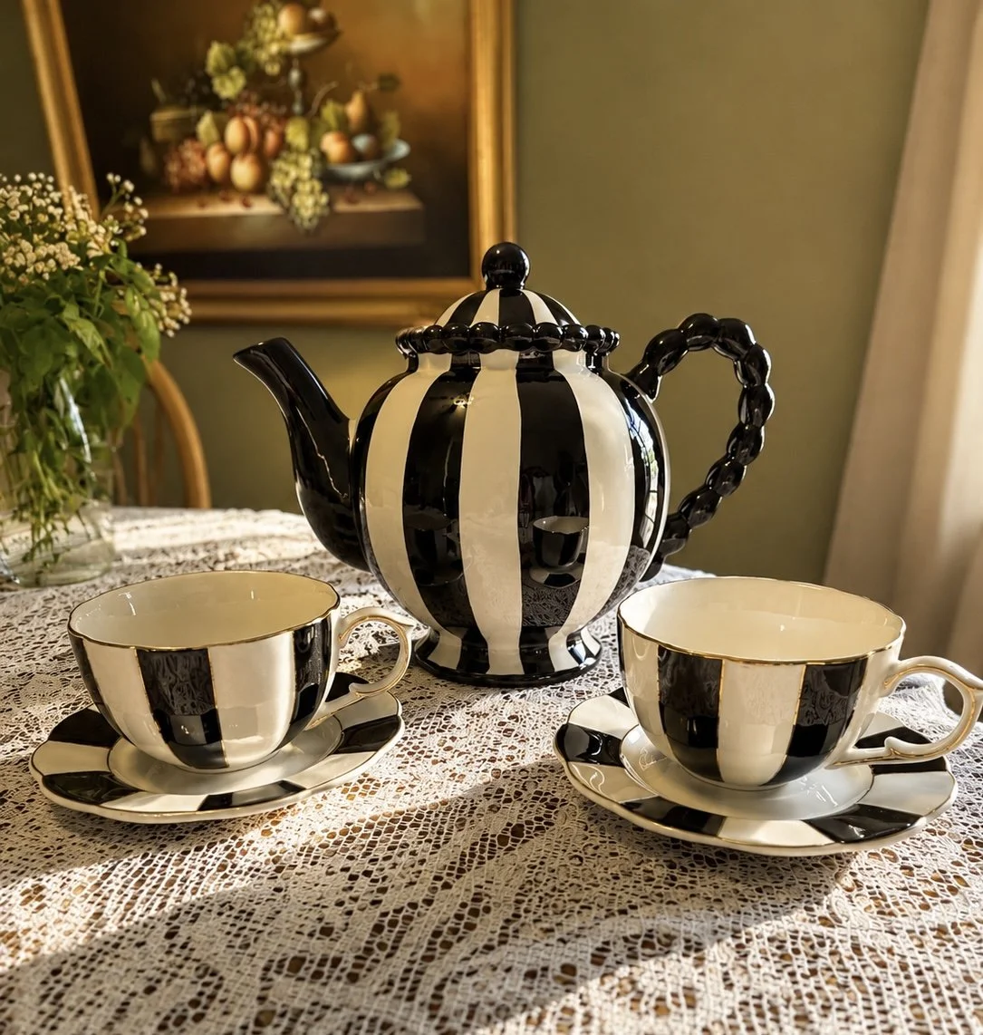 Black and white striped teapot with matching teacups and saucers on a lace tablecloth.