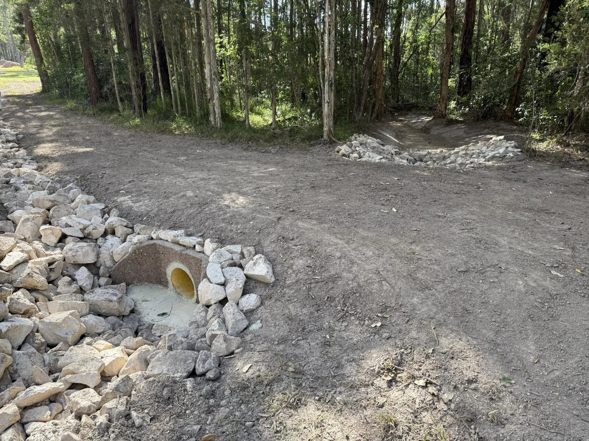 A dirt path in a forest with a pile of rocks on the side and construction markings on the ground.