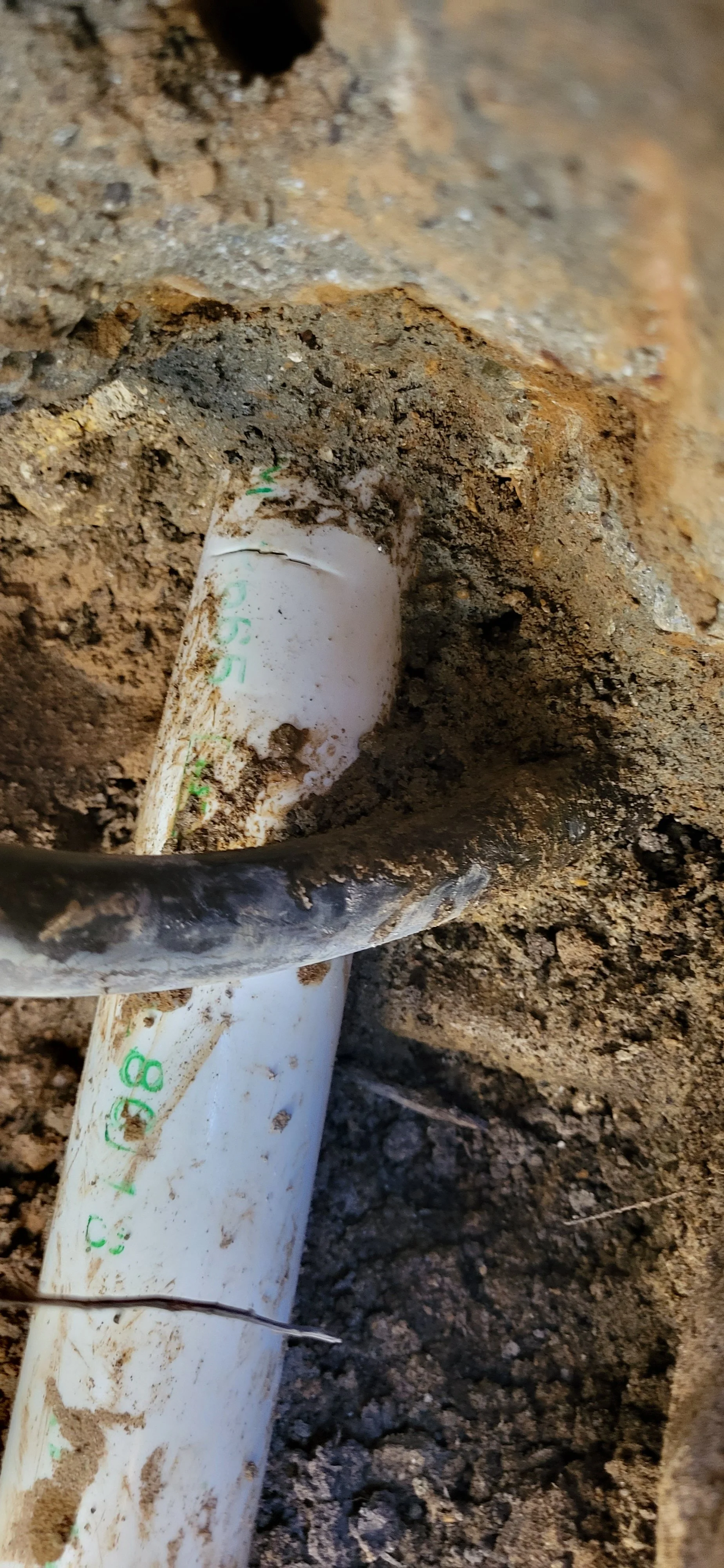 Close-up of a PVC pipe partially buried in dirt with a black cable or wire passing over it.