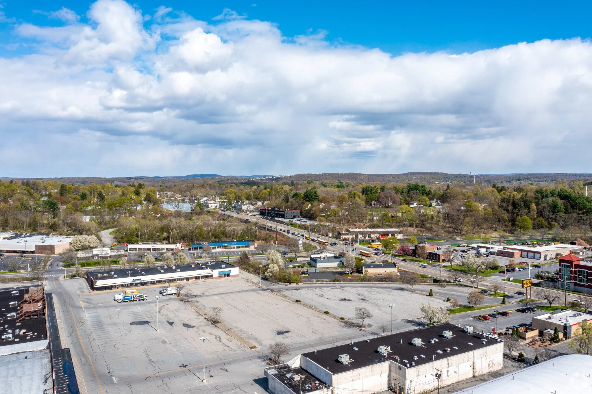 A vacant shopping plaza from above, Dutchess Center in Poughkeepsie, NY on a blue sky day. White puffy clouds and green trees in the background.