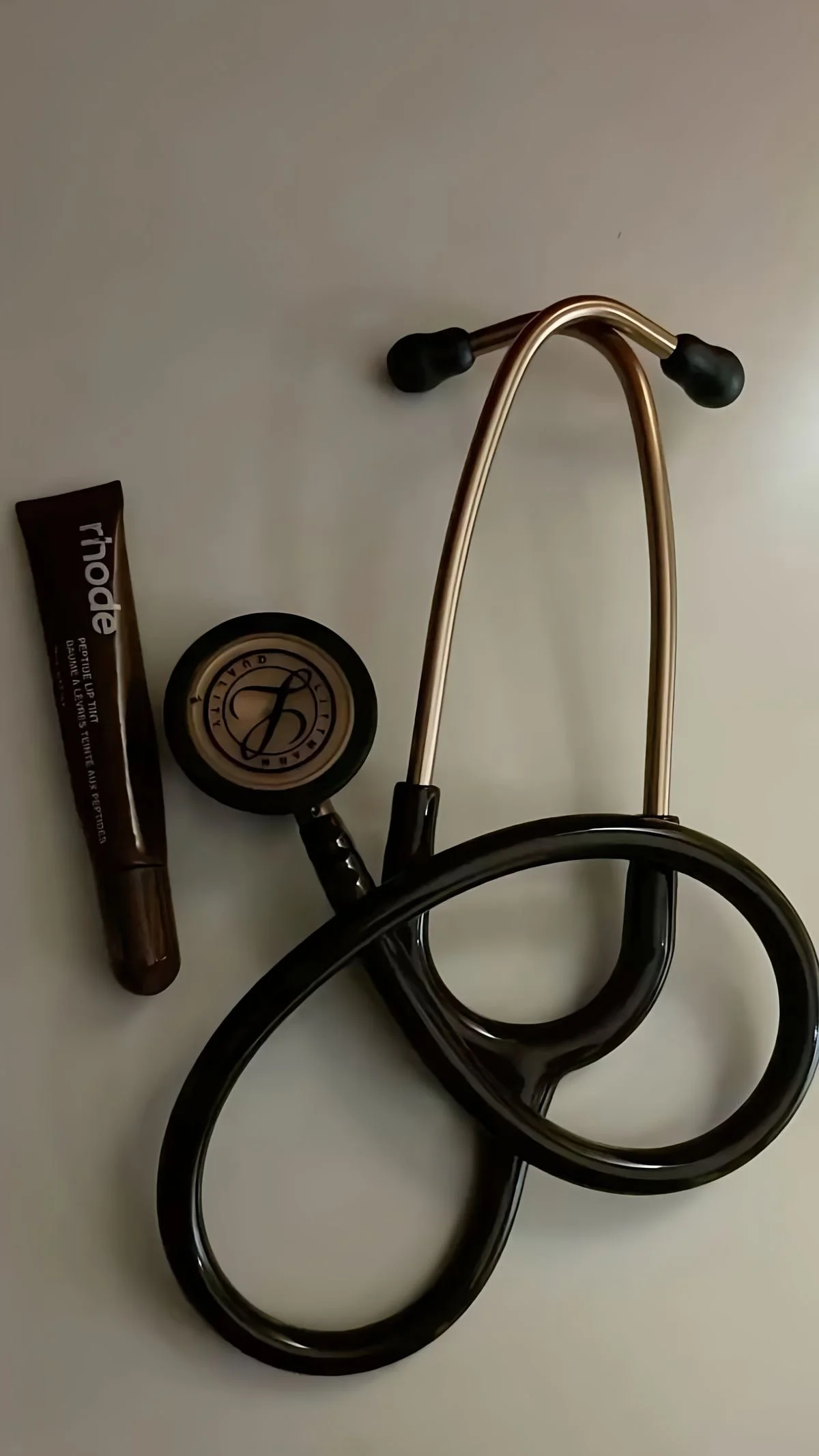 A stethoscope, a tube of Blistex lip balm, and a small container of BareMinerals makeup on a white surface.