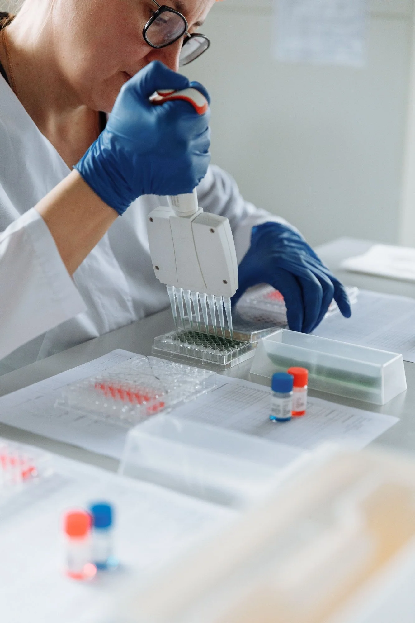 A scientist in protective gloves and glasses using a pipette to transfer liquid in a laboratory with test tubes and laboratory supplies on the table.