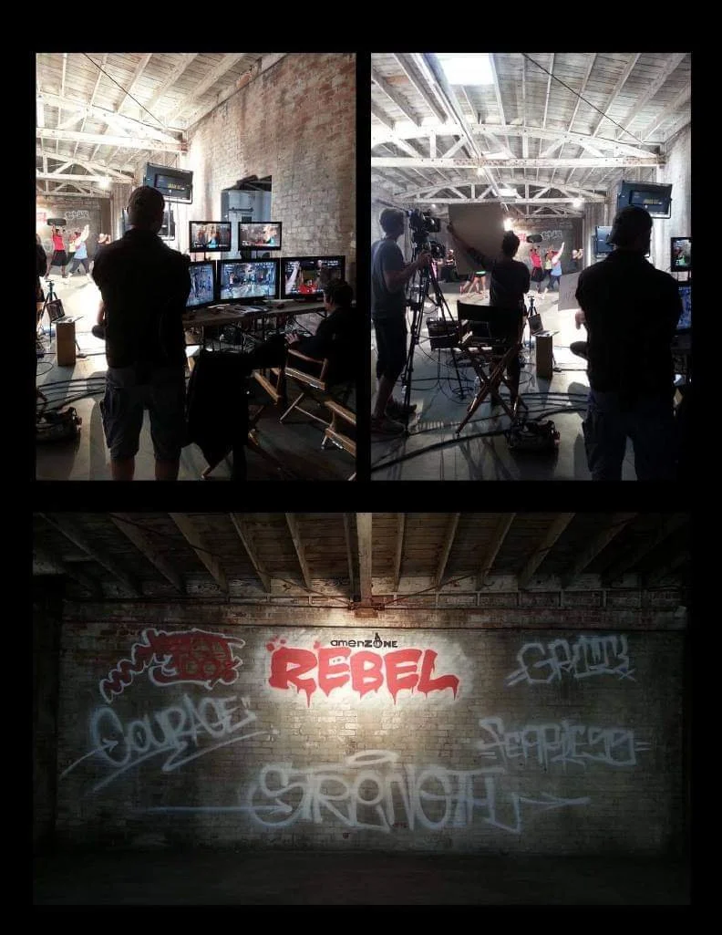 Behind-the-scenes photos of a film or video production set inside an industrial-style warehouse with exposed brick walls and wooden ceiling beams. The setup includes multiple monitors, cameras, and crew members filming or preparing for scene production. The lower part of the image features graffiti art on a brick wall, including the word "REBEL" painted in red, along with other graffiti tags.