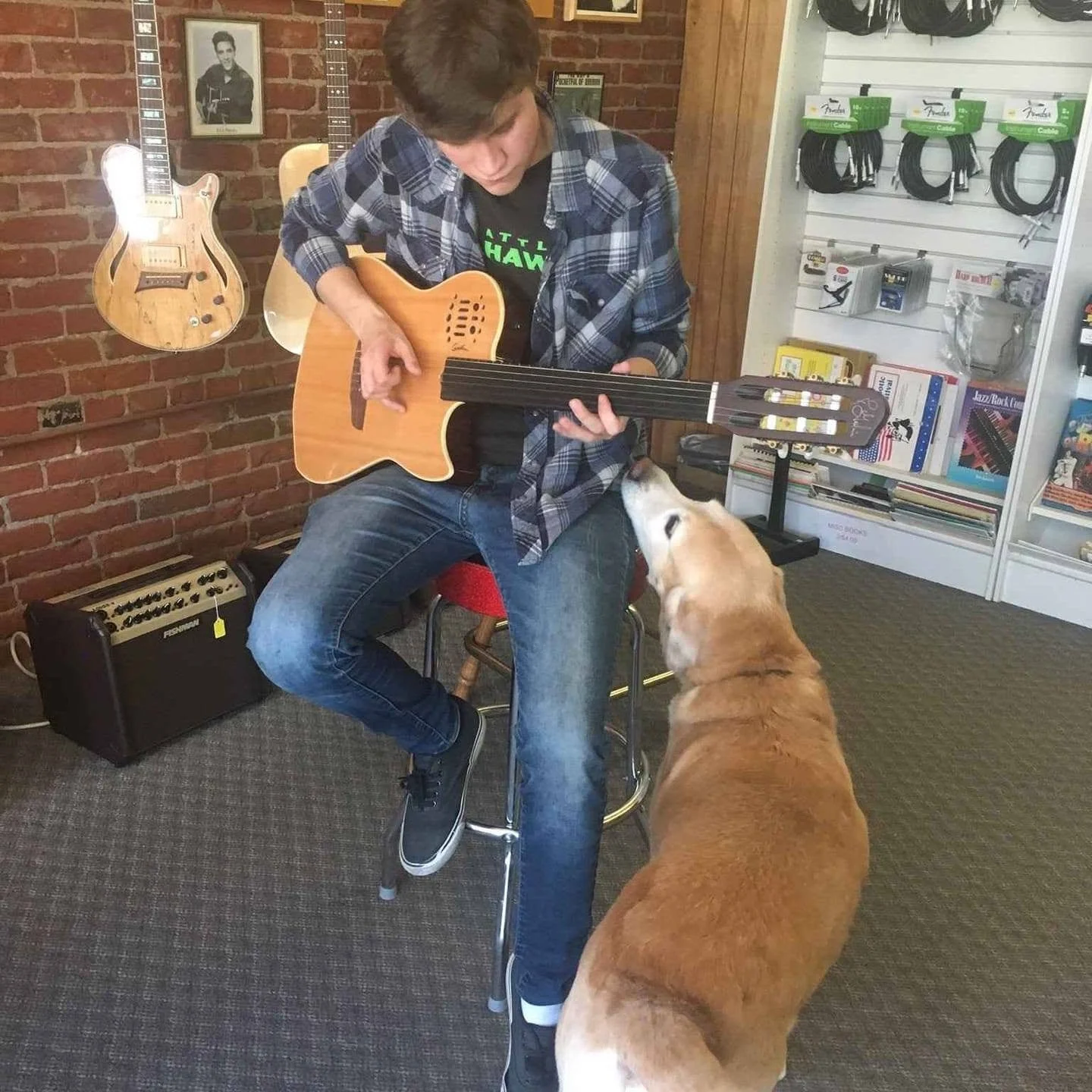 Bronson Moreno playing guitar in a guitar shop while a golden retriever listens