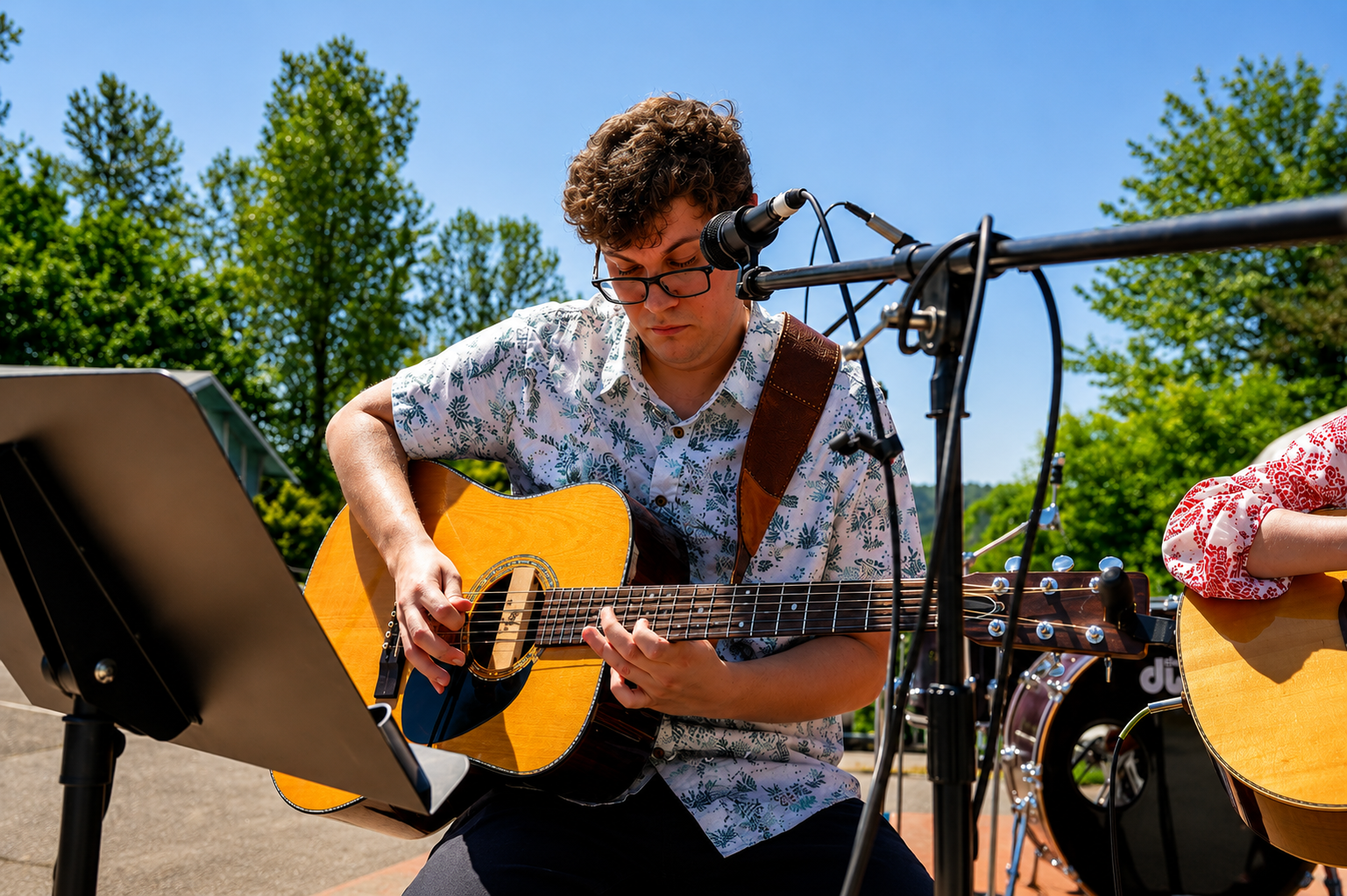 Bronson Moreno playing an acoustic guitar outdoors during daytime with trees and blue sky in the background.