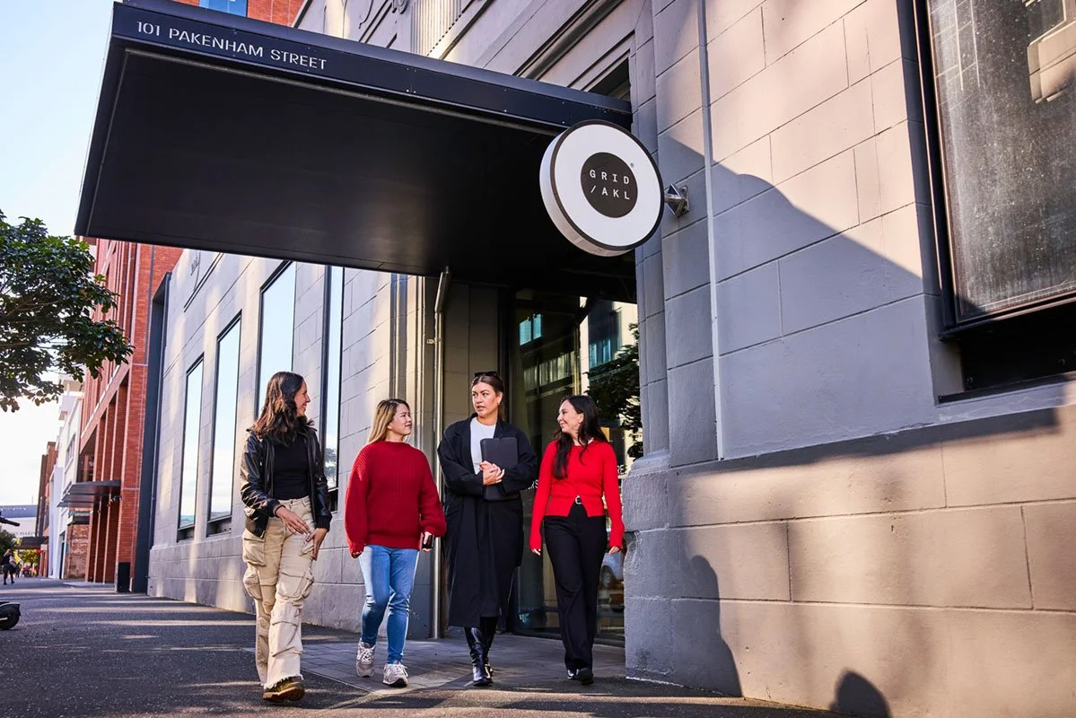 Four women walking and talking together outside a modern building with large windows and a sign that reads 'Grid AKL' at 101 Pakenham Street.