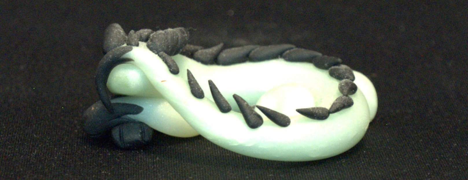 A small teal eastern dragon with black spikes on its back lying on a black surface.