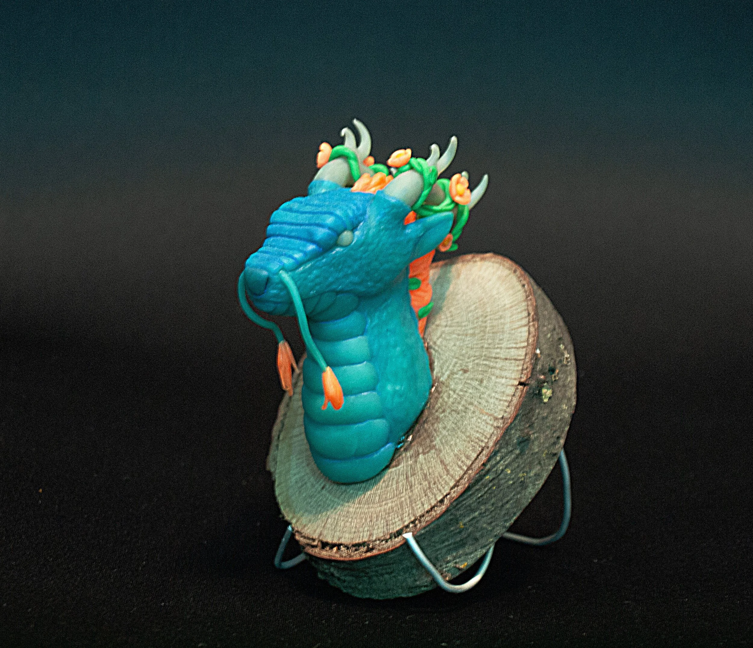 Close-up of a colorful clay model of a dragon head mounted on wood.