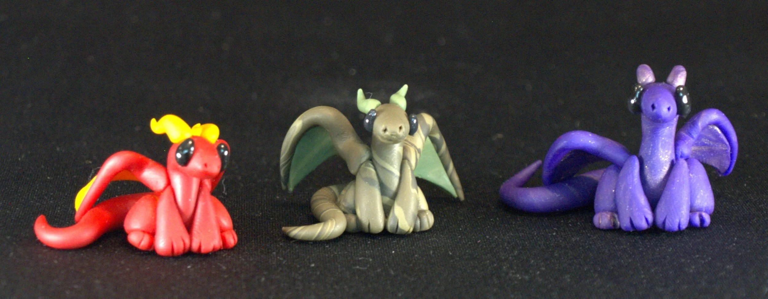 Three small dragon figurines in red, green, and purple colors on a black background.