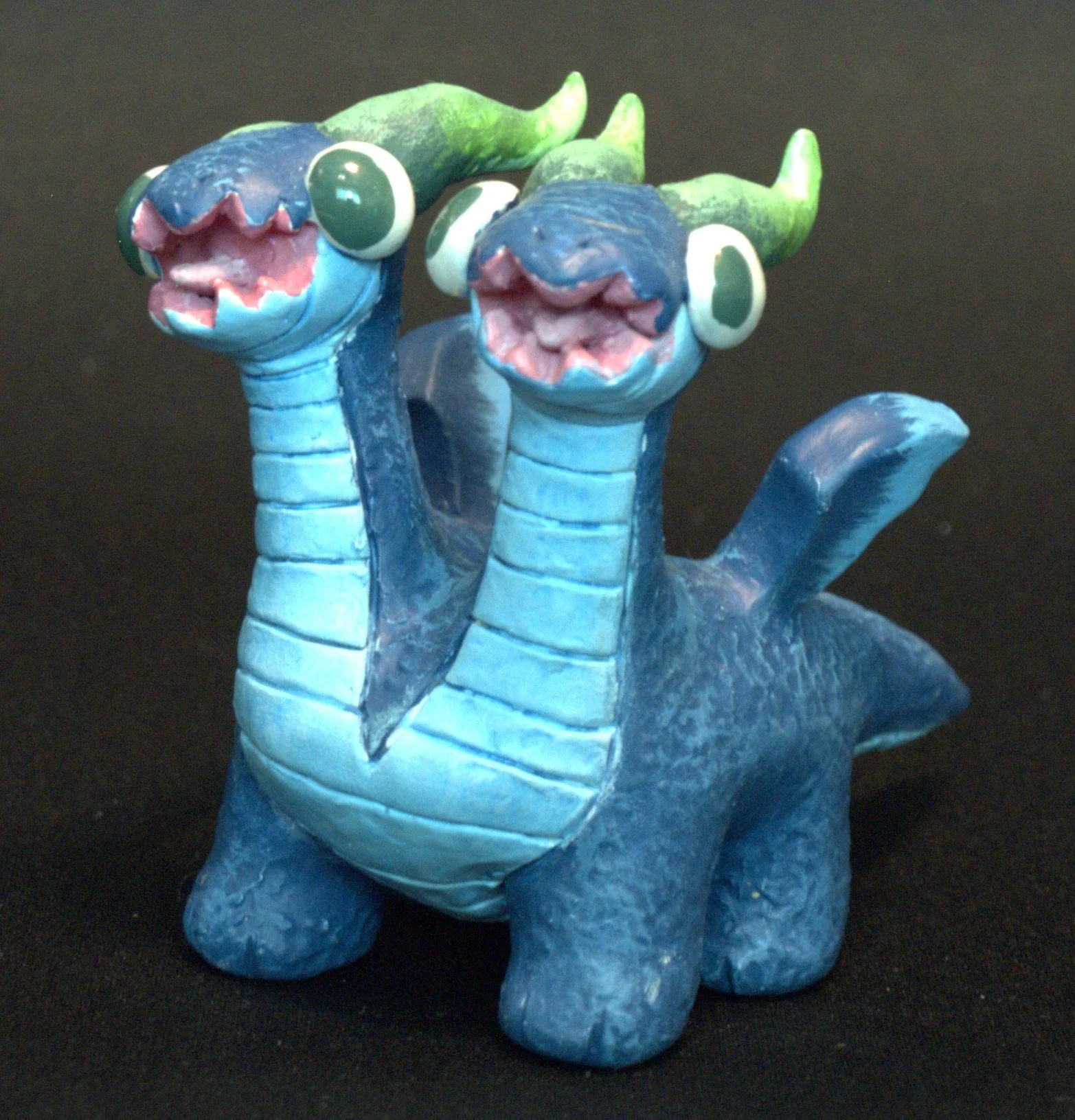A colorful dragon figurine with two heads, blue body, green horns, and big cartoonish eyes, set against a black background.
