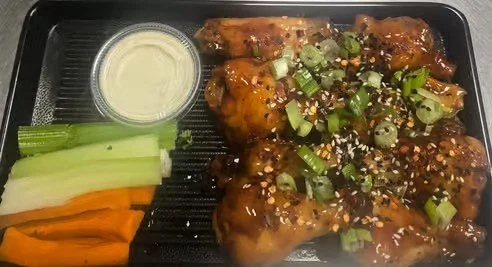 Barbecue chicken wings garnished with chopped green onions and sesame seeds, served with celery and carrot sticks, and a side of ranch dressing.