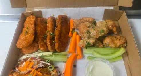 Takeout box with fried chicken wings, carrot sticks, celery sticks, and dipping sauce.