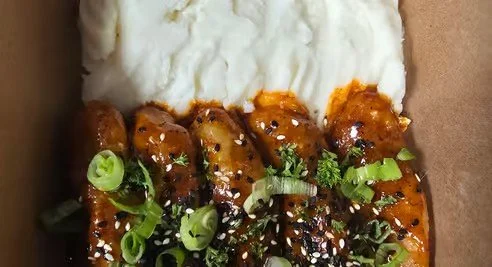 Close-up of a Japanese-style rice bowl with glazed chicken skewers topped with chopped green onions, sesame seeds, and garnished with herbs, served alongside a bed of white rice.