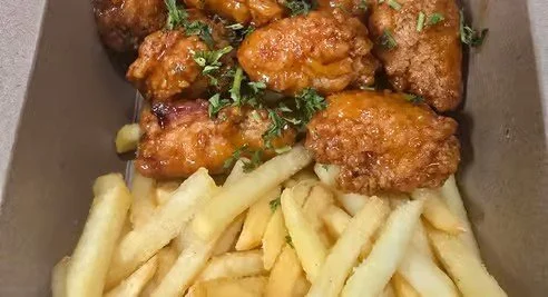 Fried chicken pieces with garnish and a side of French fries in a takeout box.