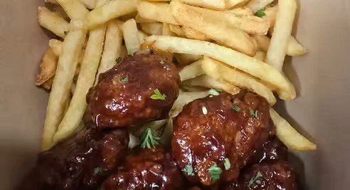 French fries and glazed meatballs garnished with parsley.