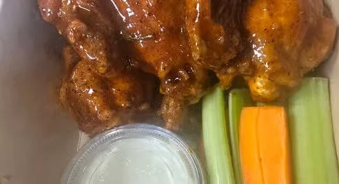 Close-up of chicken wings covered in sauce, accompanied by celery and carrot sticks, and a small container of ranch dressing.
